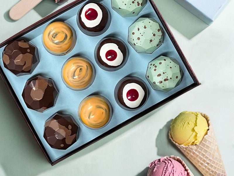 The Ice Cream Truck Collection: a box of twelve pastel summer bonbons with a chocolate paleta and ice cream cones on a soft blue-green surface