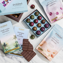 Load image into Gallery viewer, Origins Chocolate Gift Box items on marble: open bonbon box, single origin bars, and cherry and almond pouches
