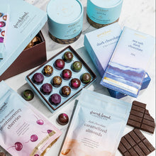 Load image into Gallery viewer, Dark Chocolate Lovers' Gift Box contents on marble: open bonbon box, hot chocolate canisters, bars, and treat pouches
