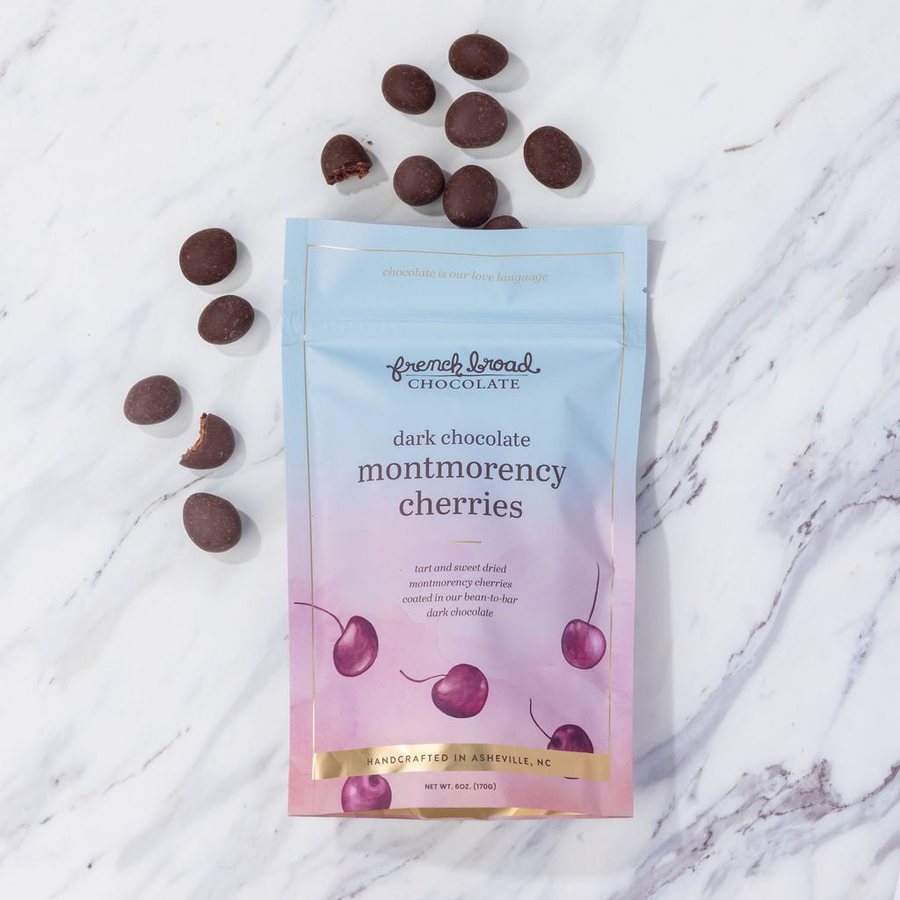 A pouch of dark chocolate covered Montmorency cherries with cherries scattered on marble
