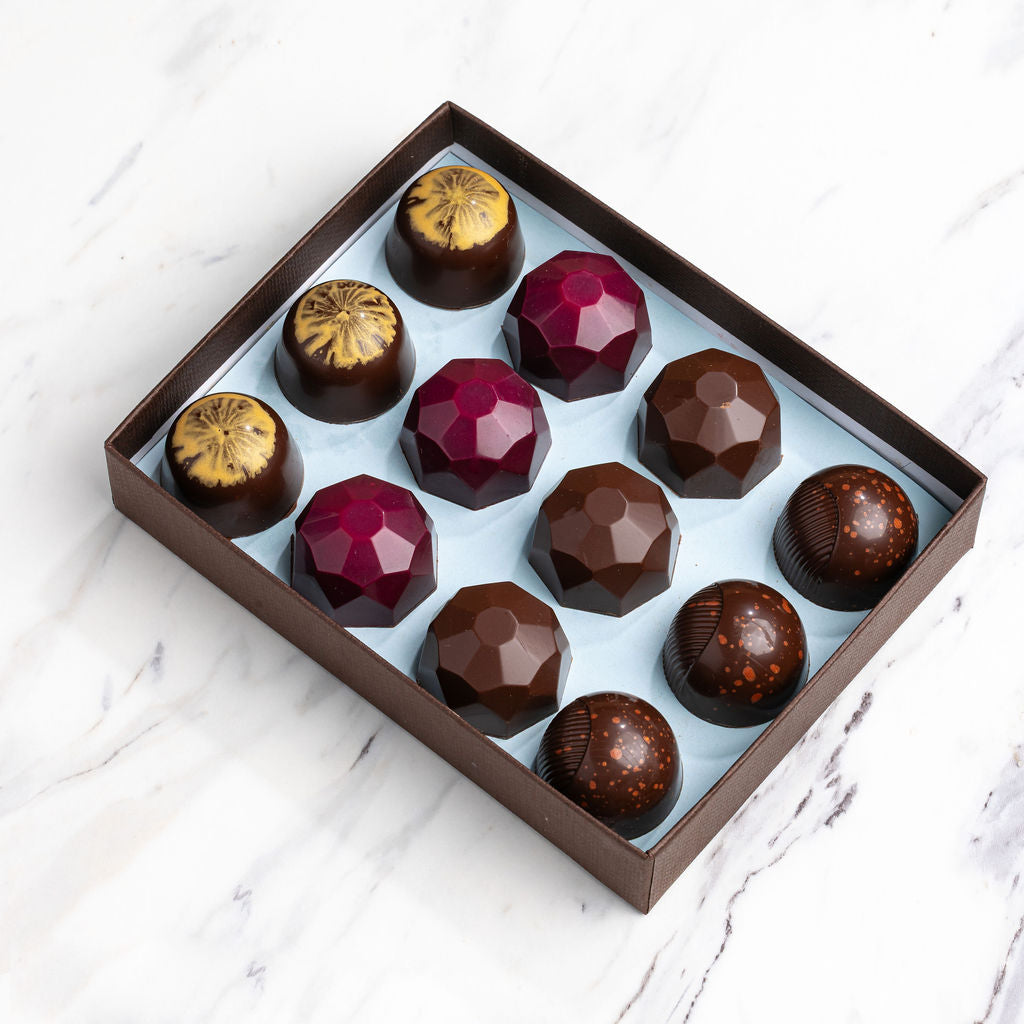 An open French Broad bonbon gift box of jewel-toned bonbons on marble, ready to celebrate