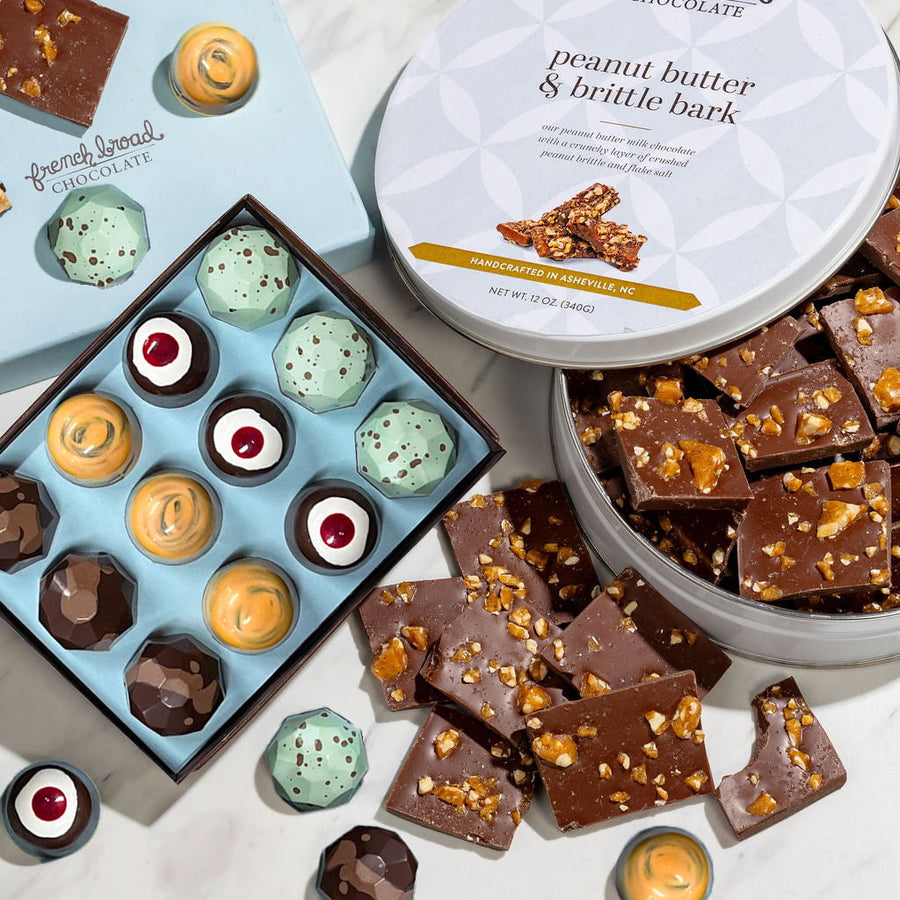 A French Broad gift set: an open box of Ice Cream Truck bonbons beside a peanut butter and brittle bark tin on marble